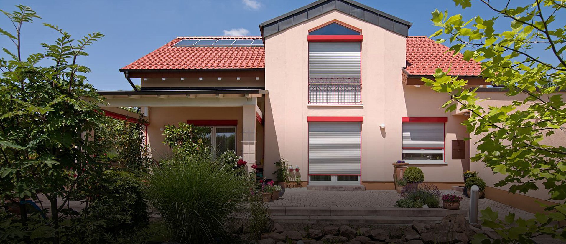 Ein hellpinkes Haus mit roten Jalousiekästen